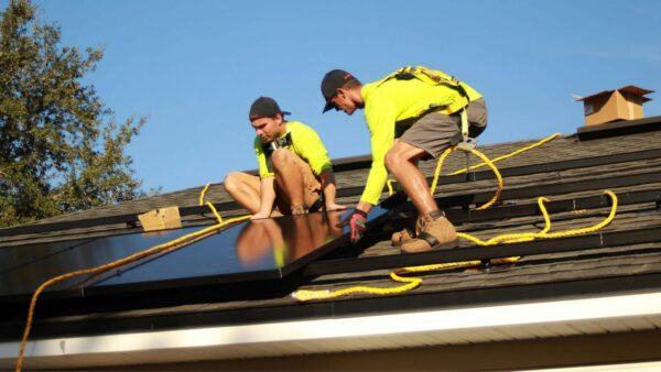 Zwei Techniker installieren Solarmodule auf einem Hausdach bei sonnigem Wetter.