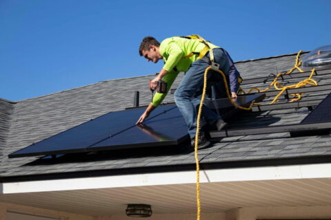 Ein Techniker installiert Solarmodule auf einem Hausdach unter klarem Himmel.