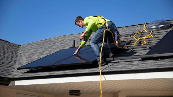 Ein Techniker installiert Solarmodule auf einem Hausdach unter klarem Himmel.