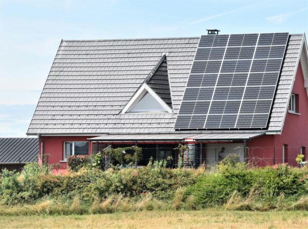 Rotes Einfamilienhaus mit großer Solaranlage auf dem Dach an einem sonnigen Tag.